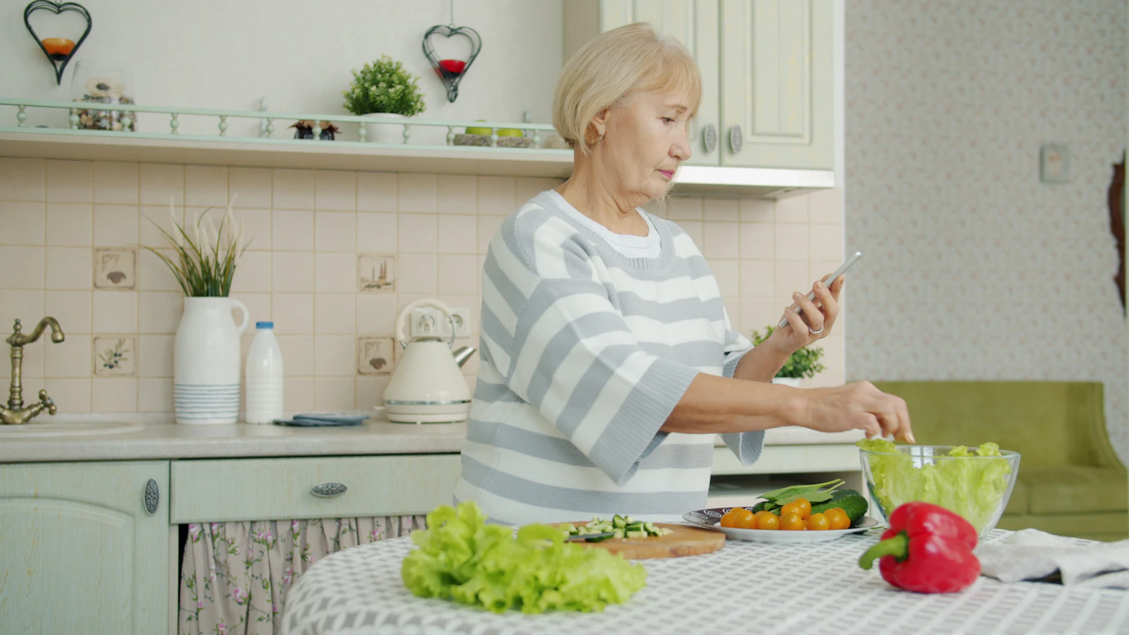 Een oudere vrouw maakt een salade klaar in een lichte keuken.