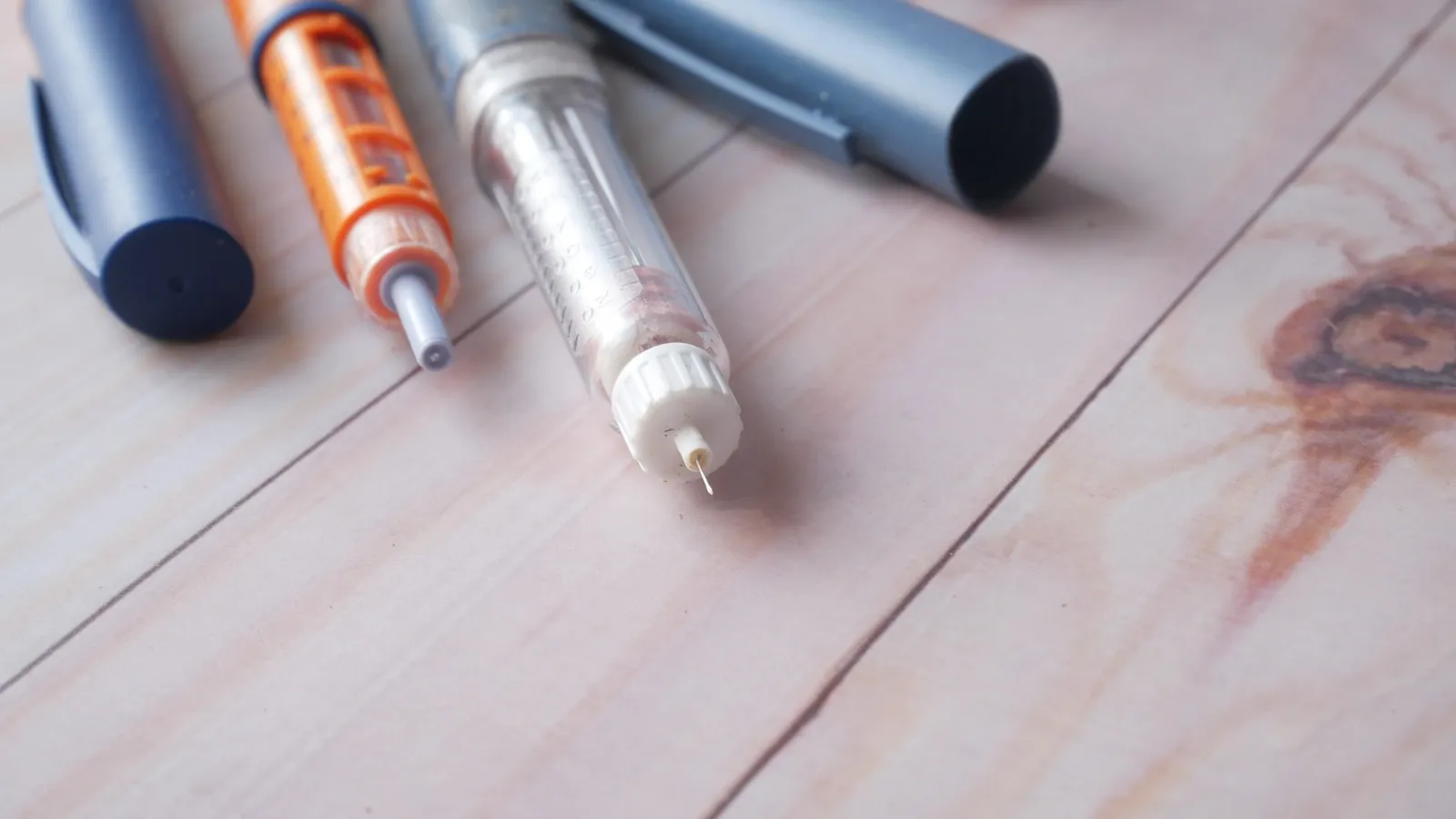 Twee injectiepennen en een spuit liggen naast elkaar op een houten tafel.