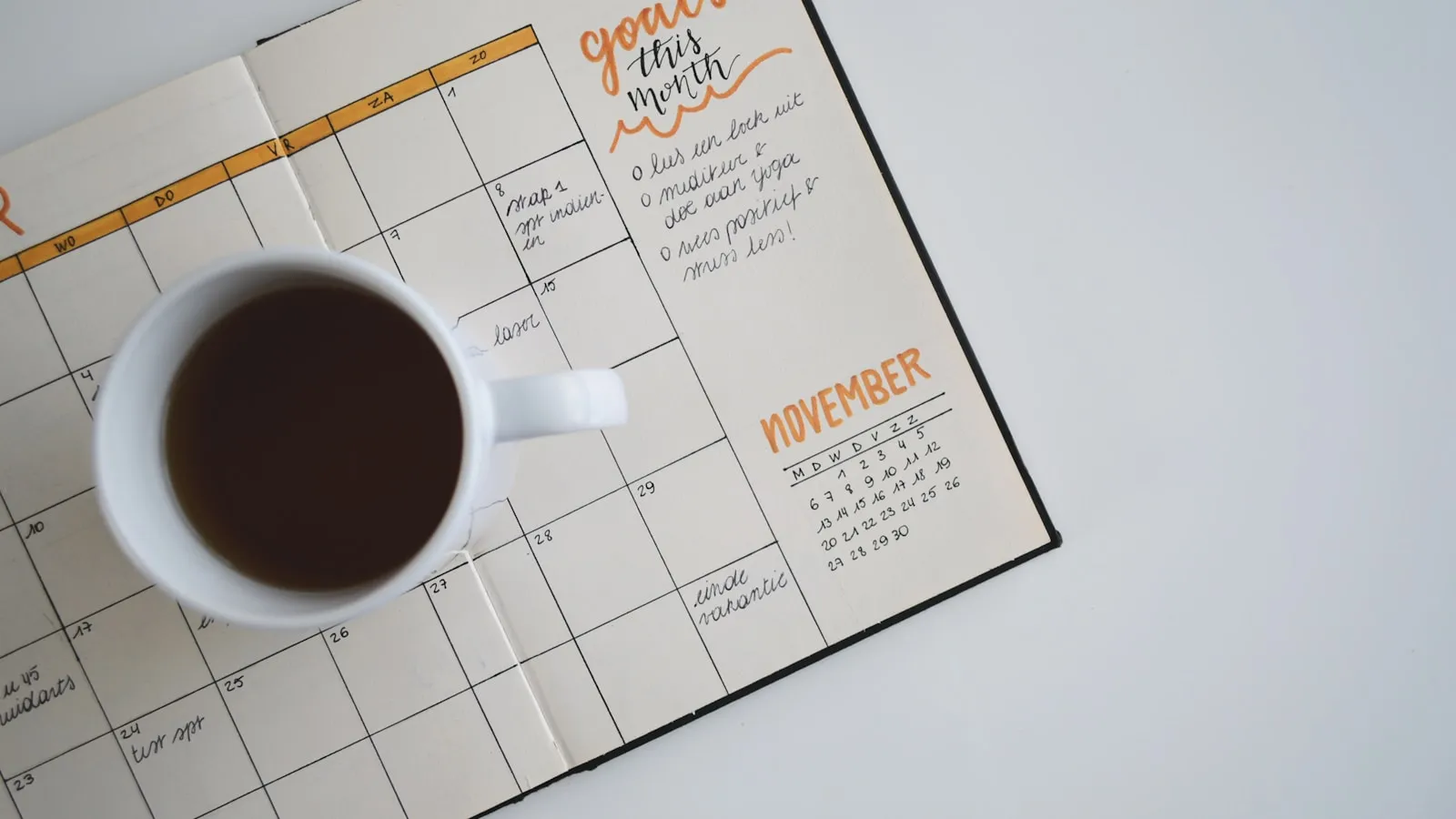 Een kop koffie staat op een opengeslagen maandplanner.