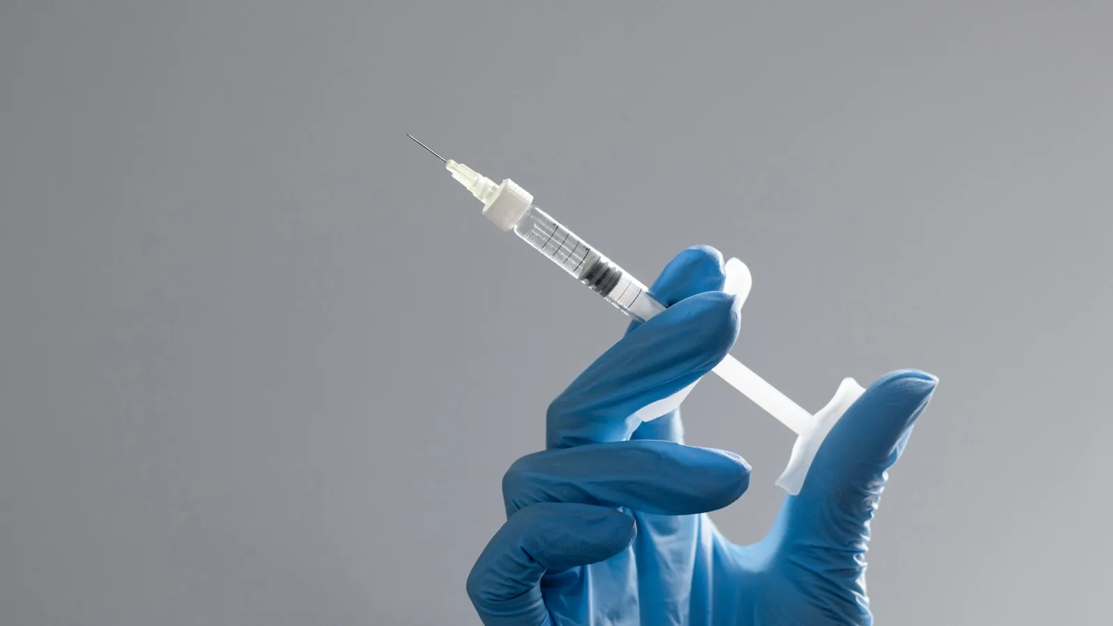 Een hand met een handschoen houdt een injectiespuit vast tegen een lichte achtergrond.