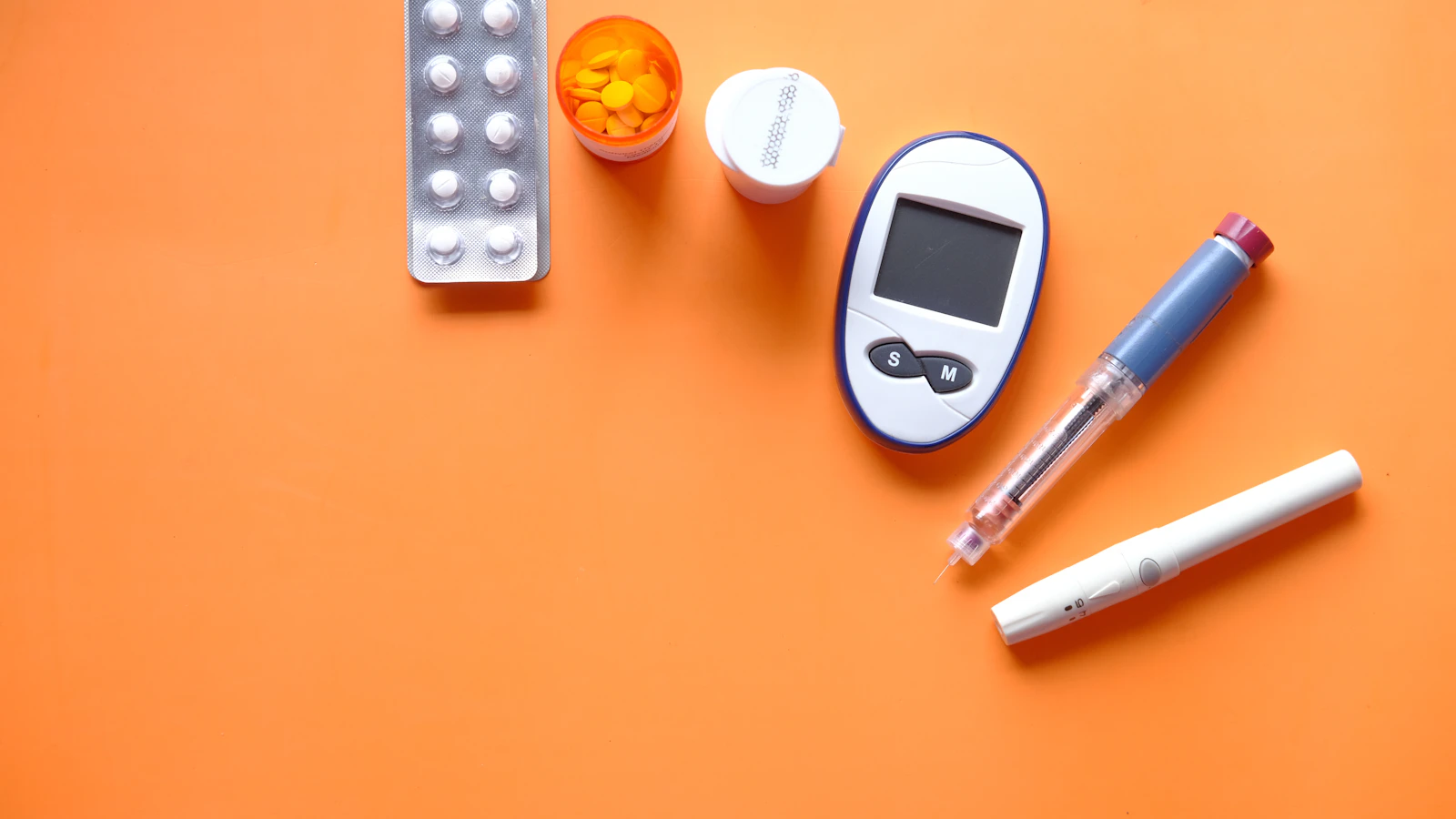 Injectiepennen, een bloedsuikermeter en doordrukstrips liggen naast elkaar op een oranje vlak.