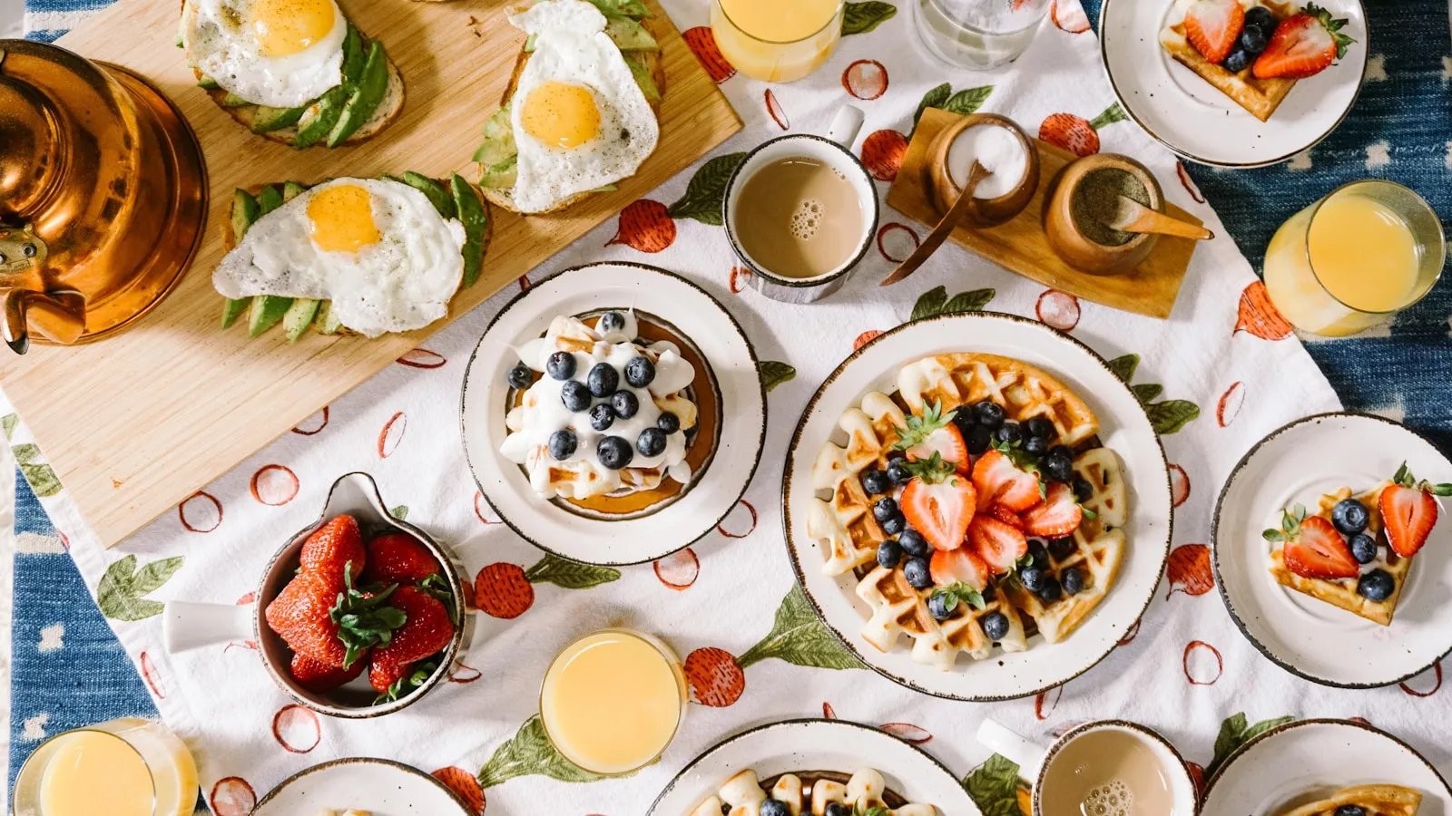 Een gedekte ontbijttafel met eieren, avocadotoast, wafels en jus d'orange.