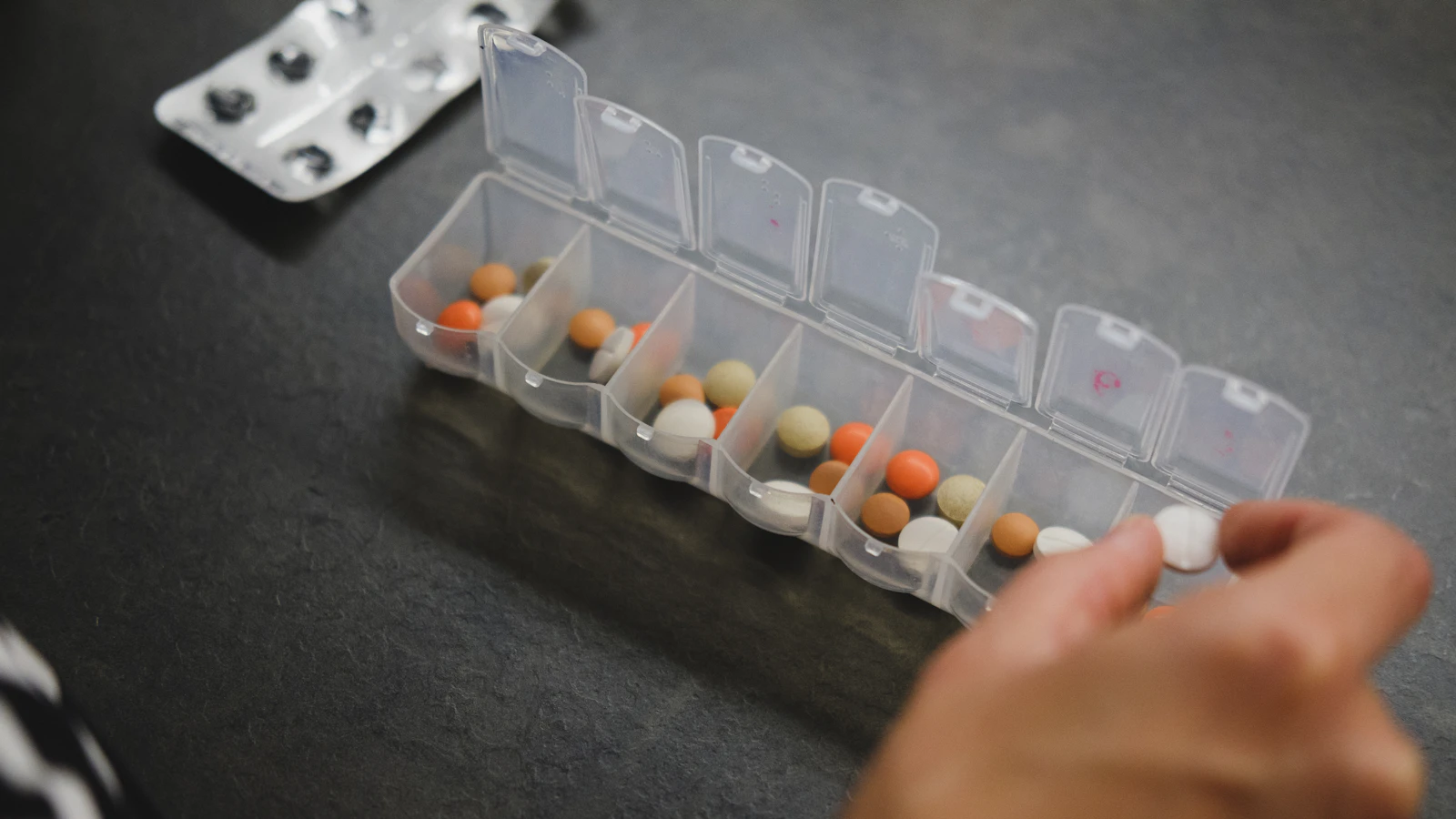 Iemand pakt een pil uit een medicijndoos.