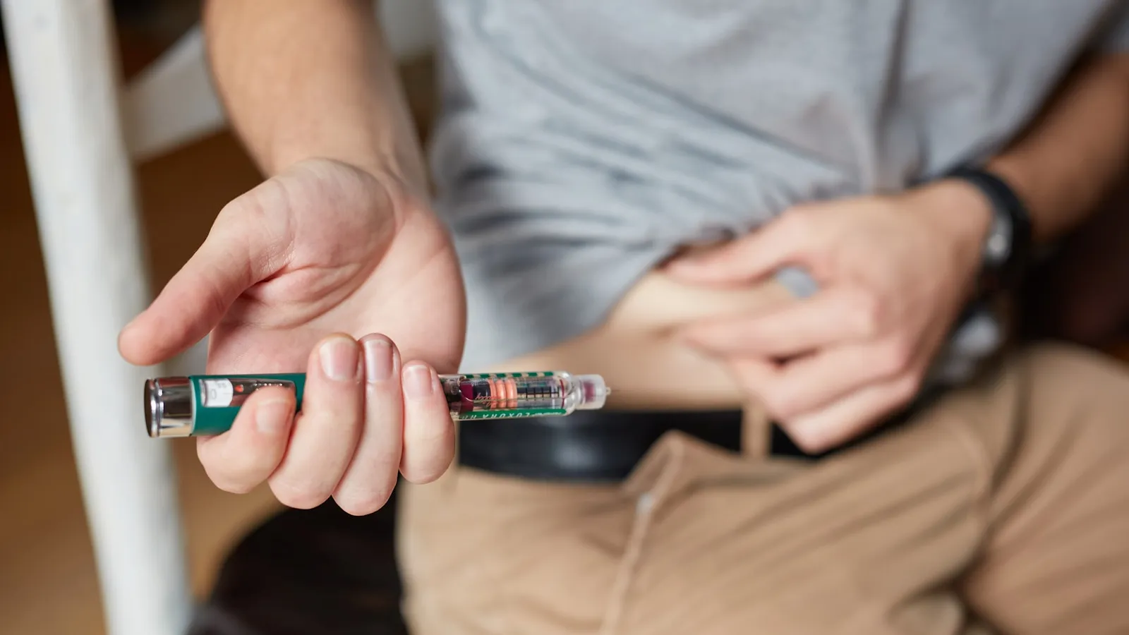 Iemand houdt een injectiepen vast en neemt een huidplooi op de buik.