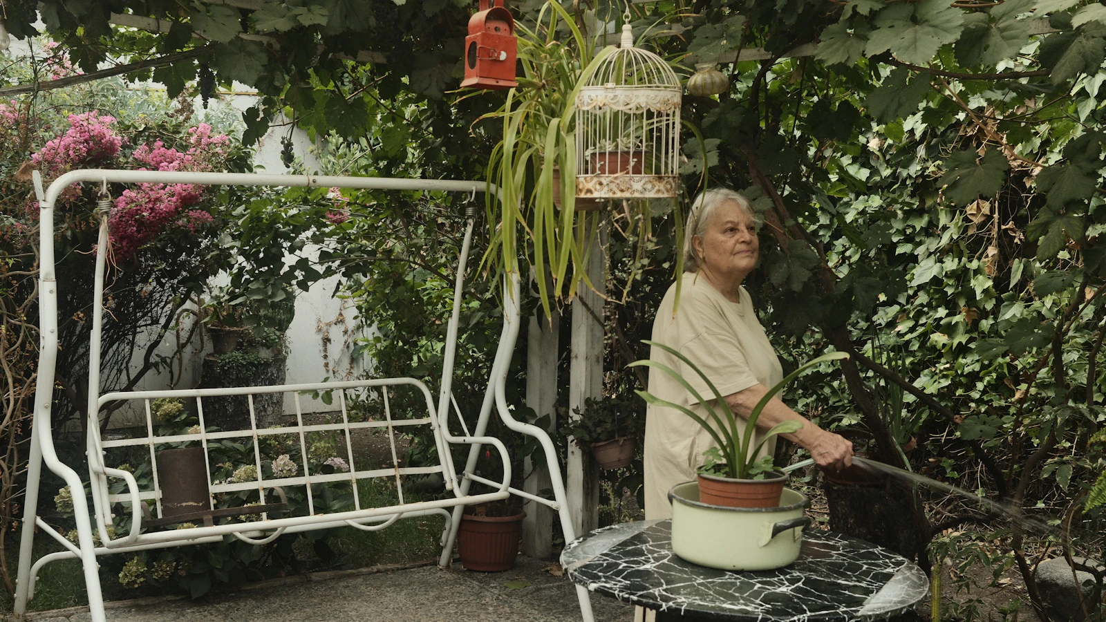 Een oudere vrouw geeft planten water in een groene tuin.