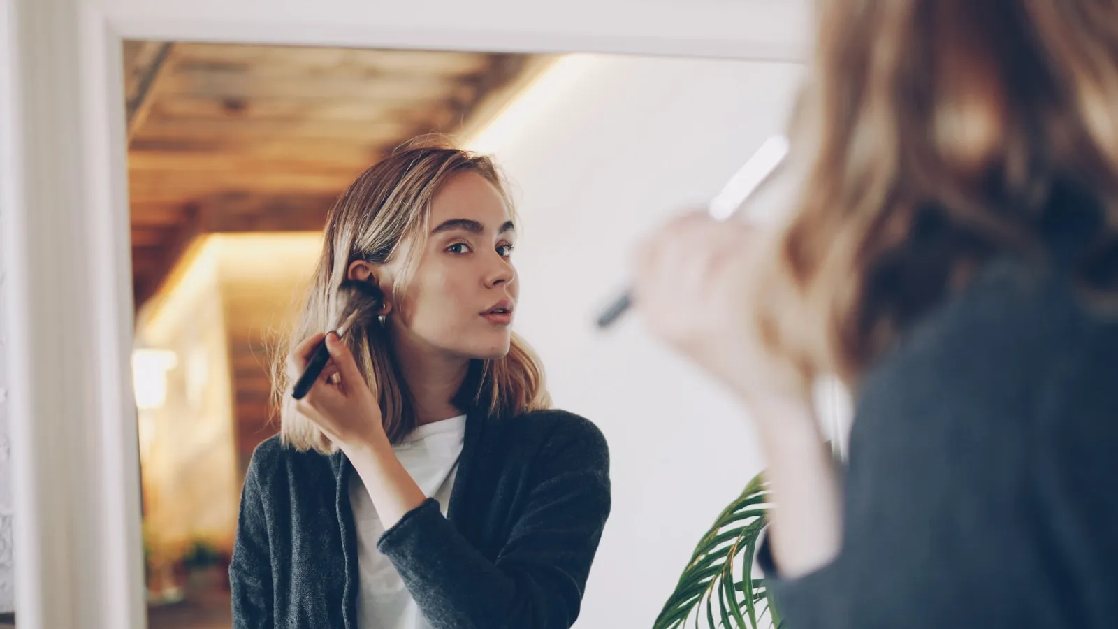 Een vrouw kamt haar haar voor een grote spiegel in een lichte kamer.