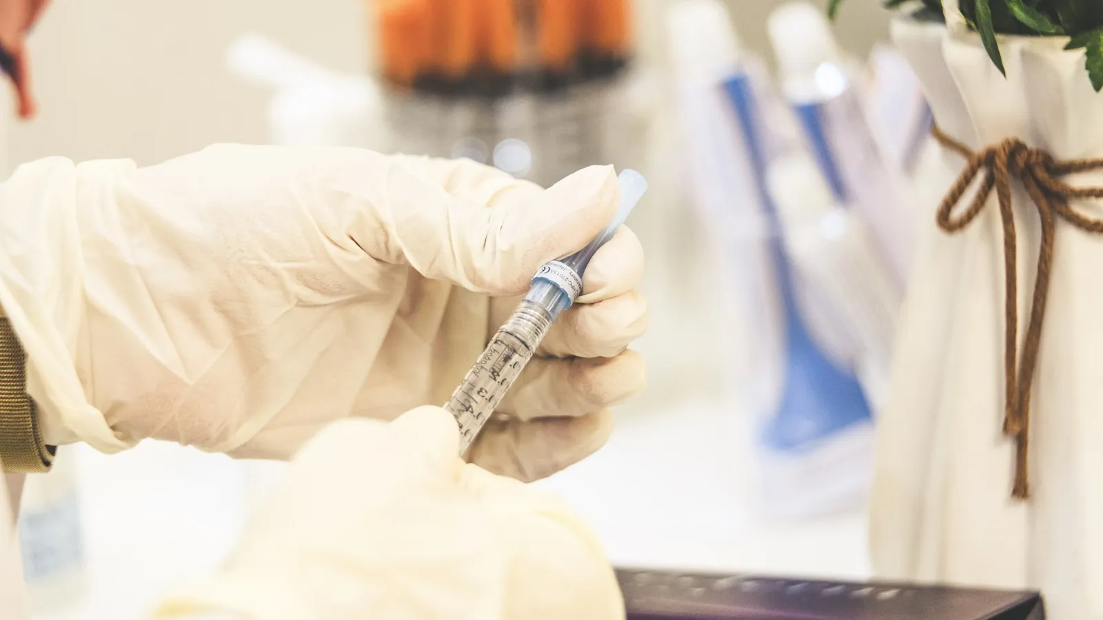 Een hand met handschoen houdt een injectiespuit vast in een lichte behandelruimte.
